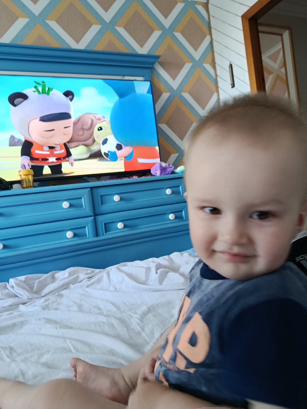 Kid in blue shirt smiles at camera, TV in background