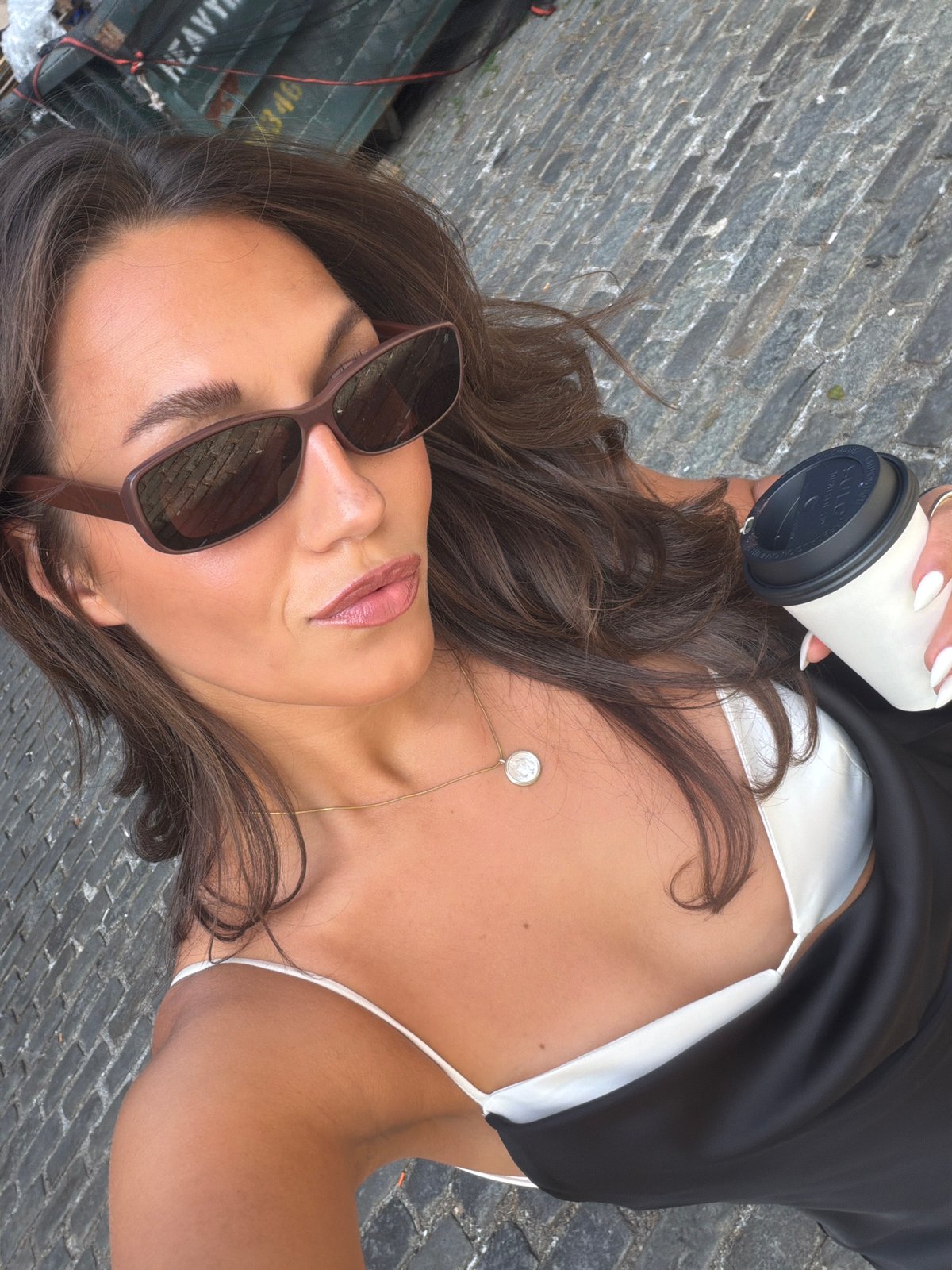 Woman takes selfie with coffee on NYC cobblestone street