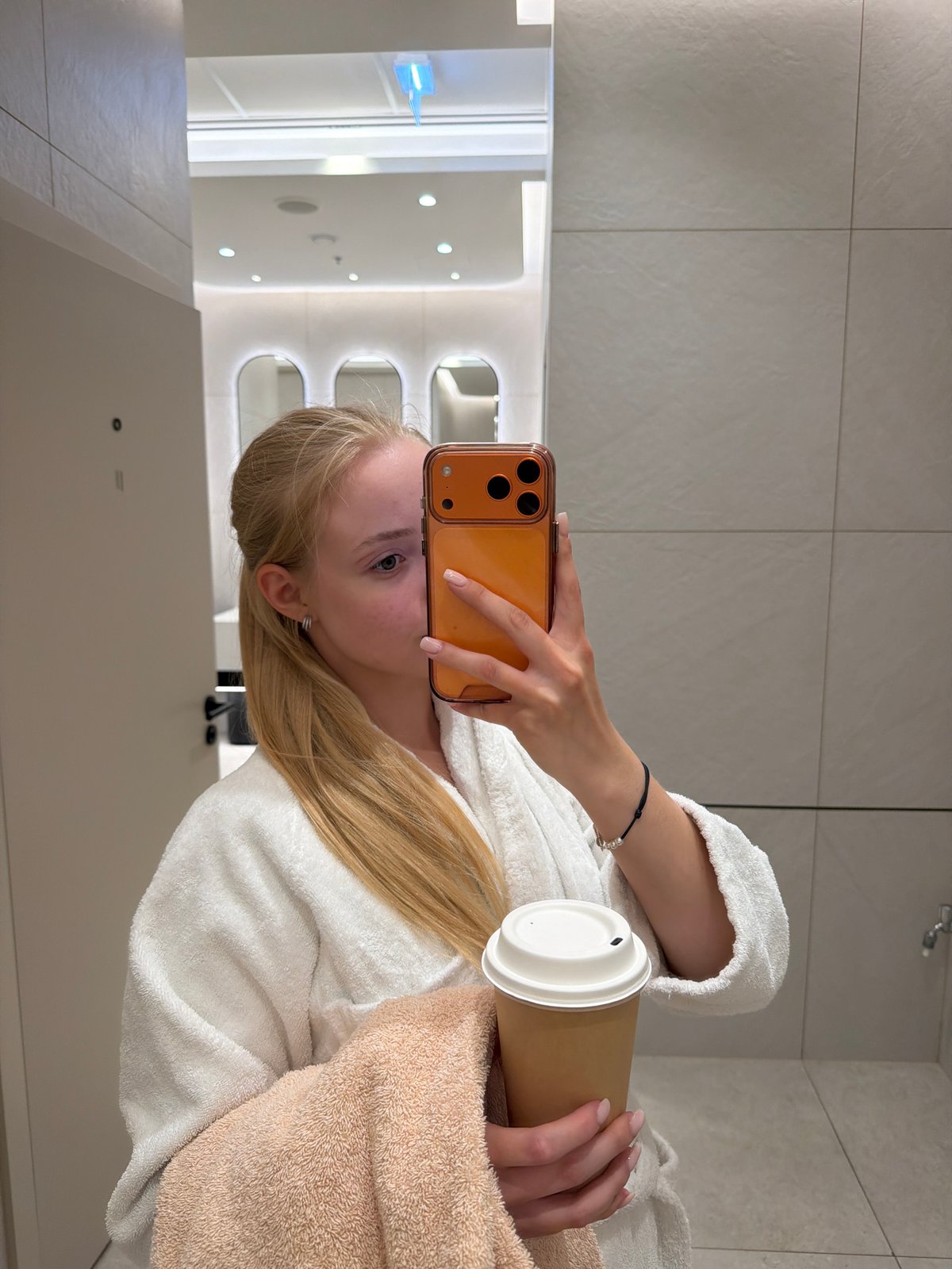 Woman takes bathroom selfie while holding coffee cup