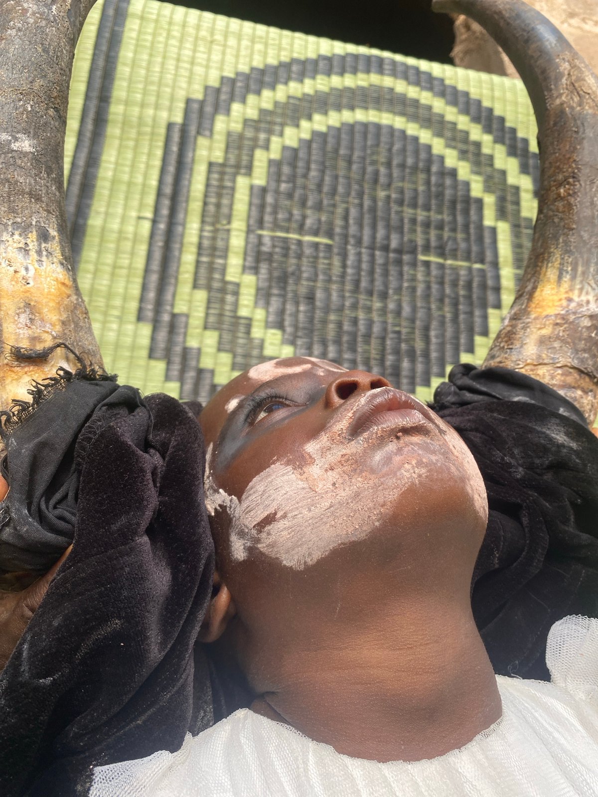 Child in traditional dress rests near ceremonial items Nigeria