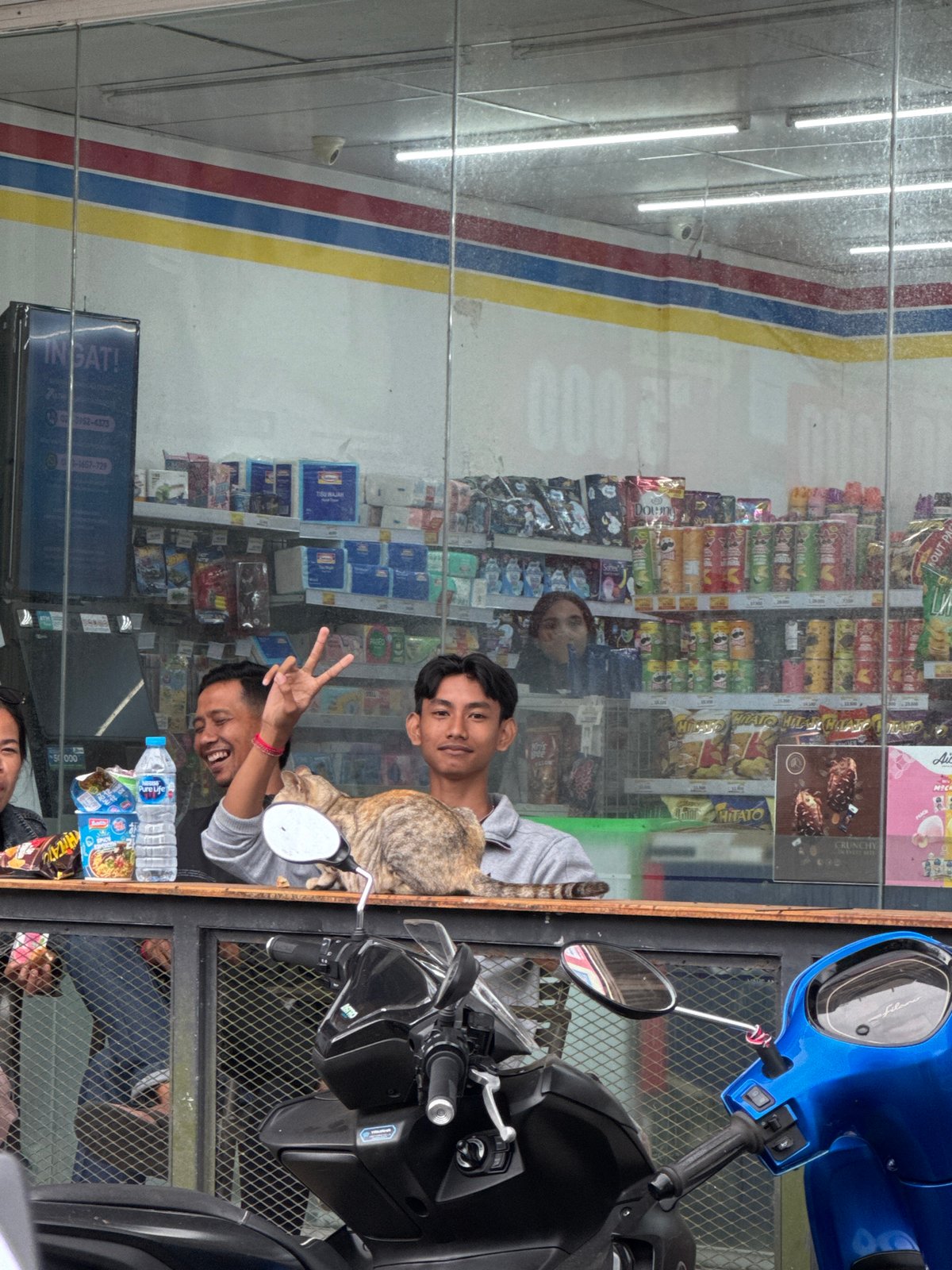 Two men pose outside Kintamani storefront with motorcycle, cat