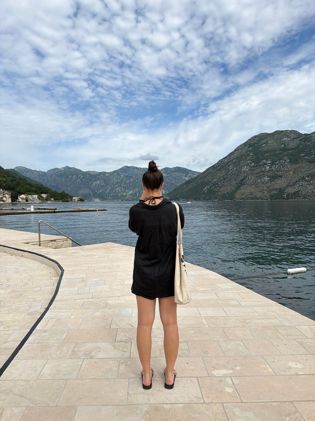 Woman walks waterfront promenade in Prčanj, Montenegro morning scene