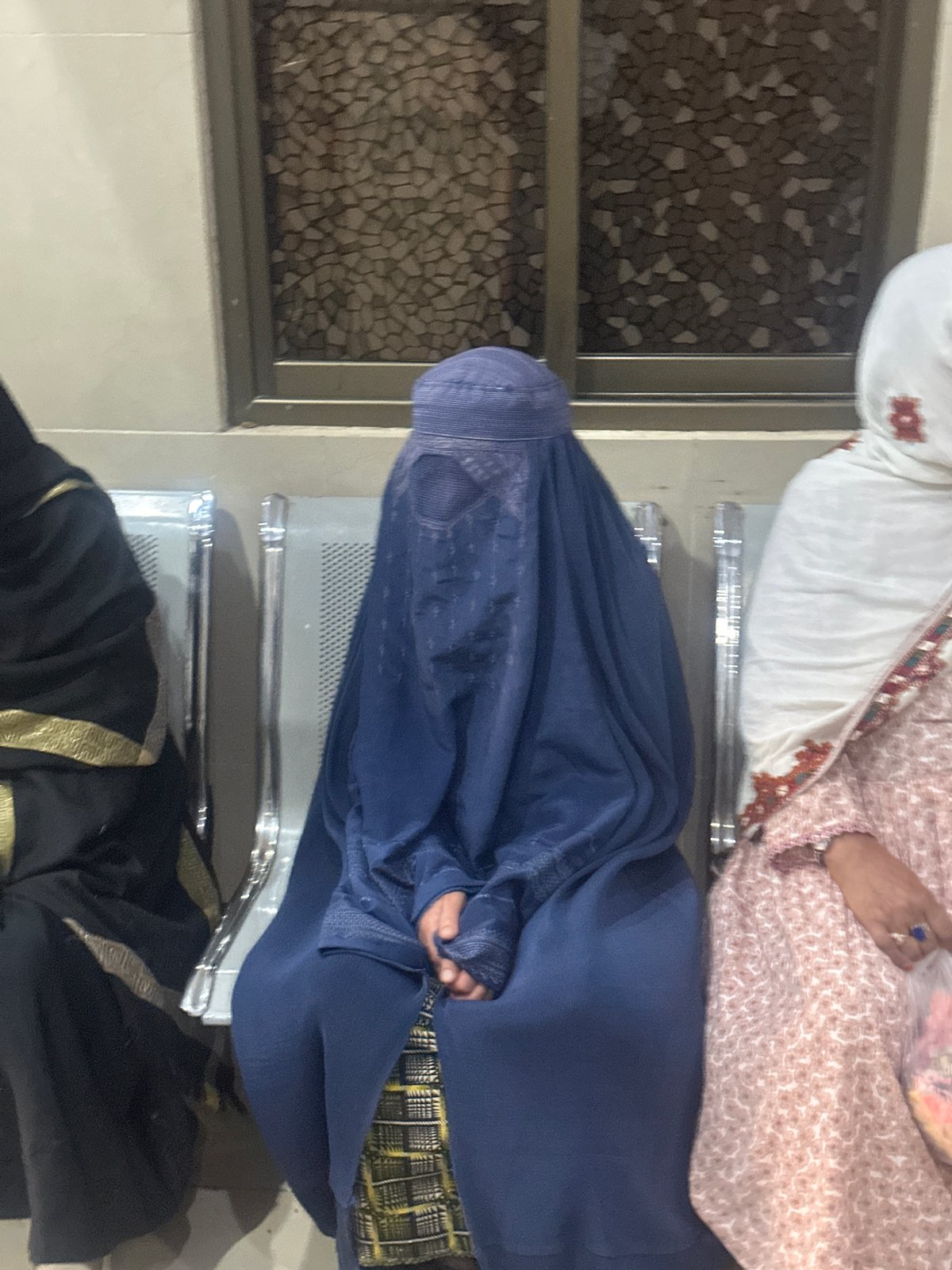 Three people seated together in Quetta, one in full burqa