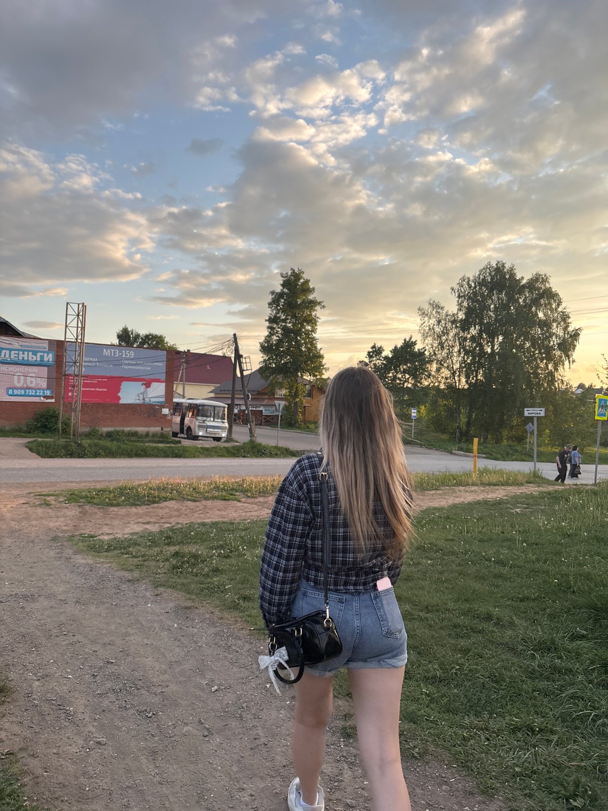 Woman walks dirt path at sunset in rural Russia