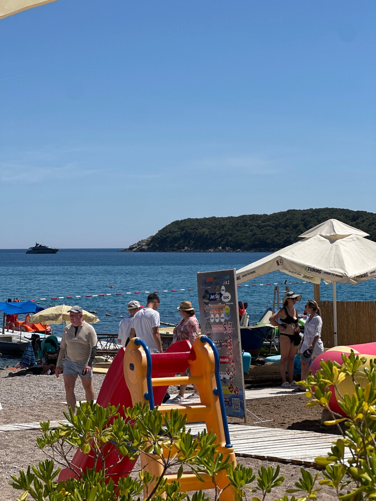Busy beach day at a Montenegrin coastal spot with inflatables and café