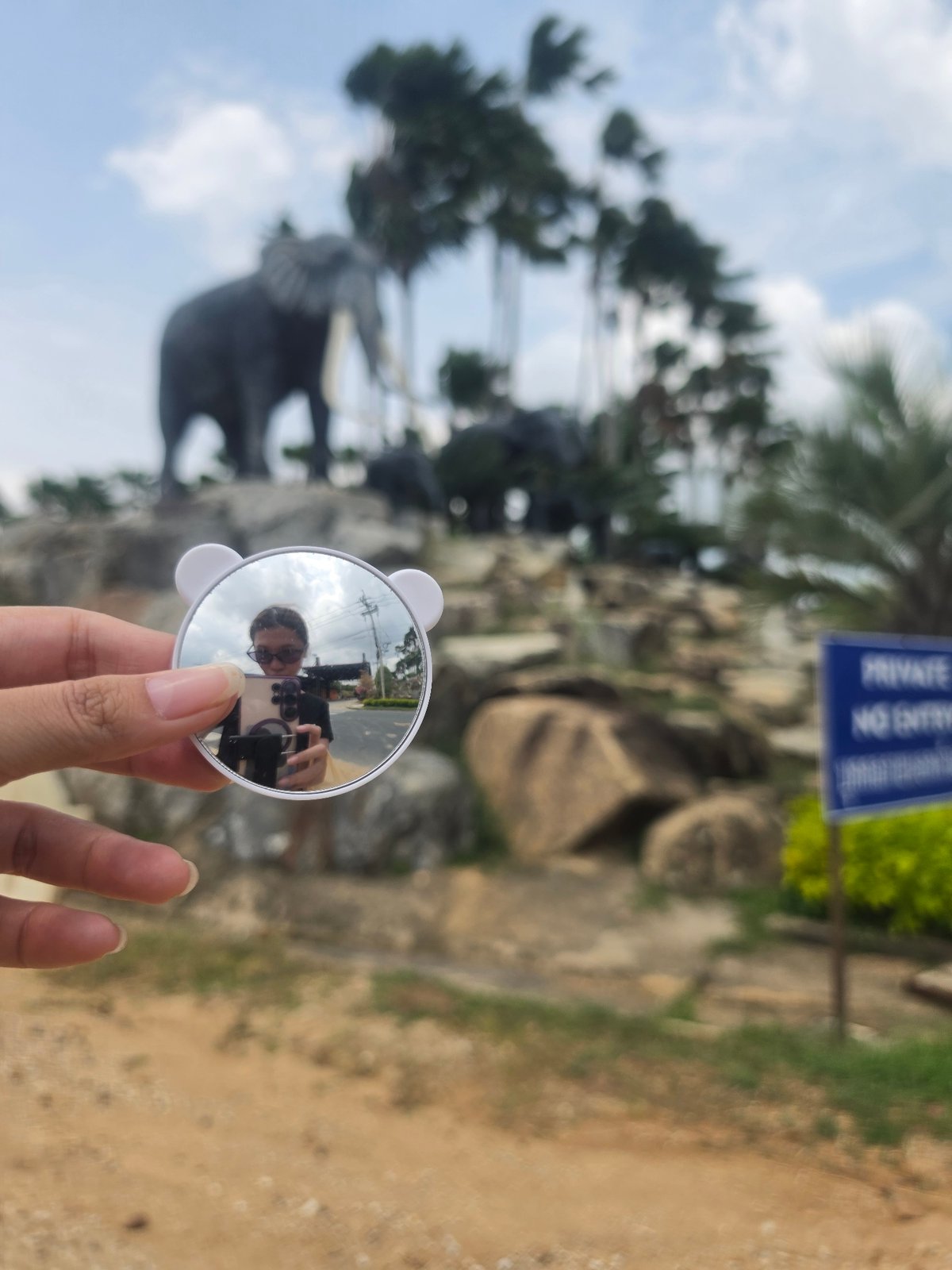Tourist photographs elephant statues at Thai temple using novelty mirror