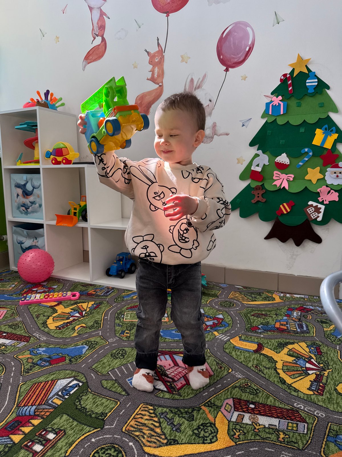 Child plays with toys on street-pattern rug in Rusanovo