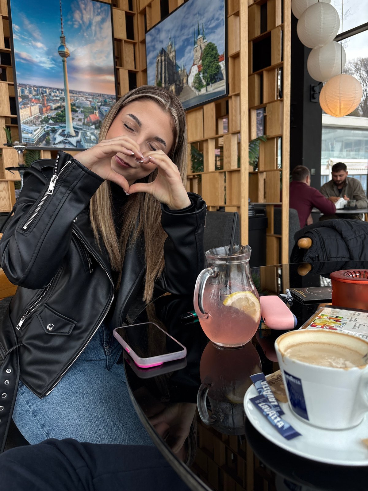 Woman makes heart gesture at cafe table with drinks