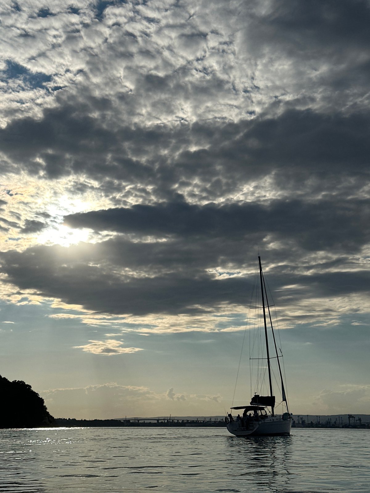 Sailboats gather near a forested hillside with a tower above