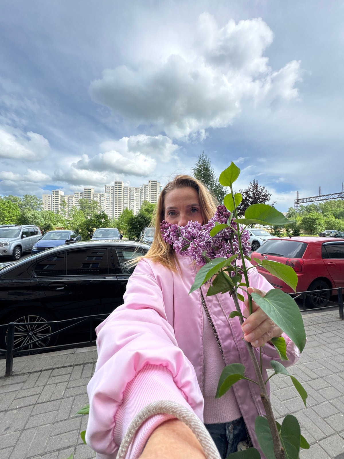 Woman poses with lilac branch in Sinyavino residential street