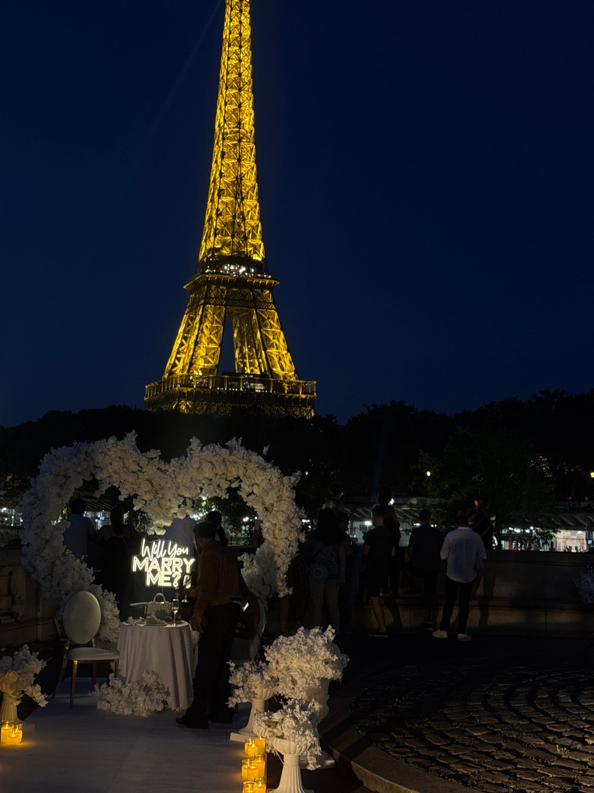Nighttime proposal setup at Champ de Mars, Eiffel Tower glowing behind