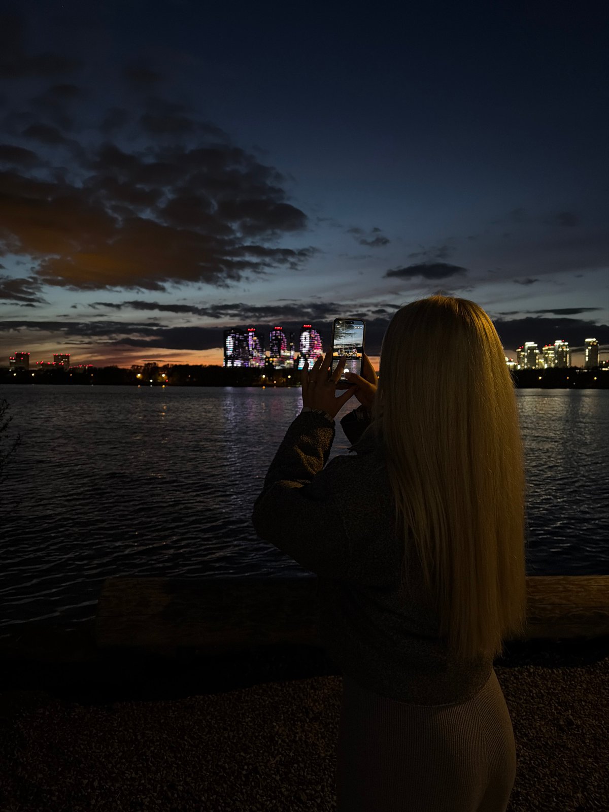 Woman photographs illuminated Kazan Family Center at night