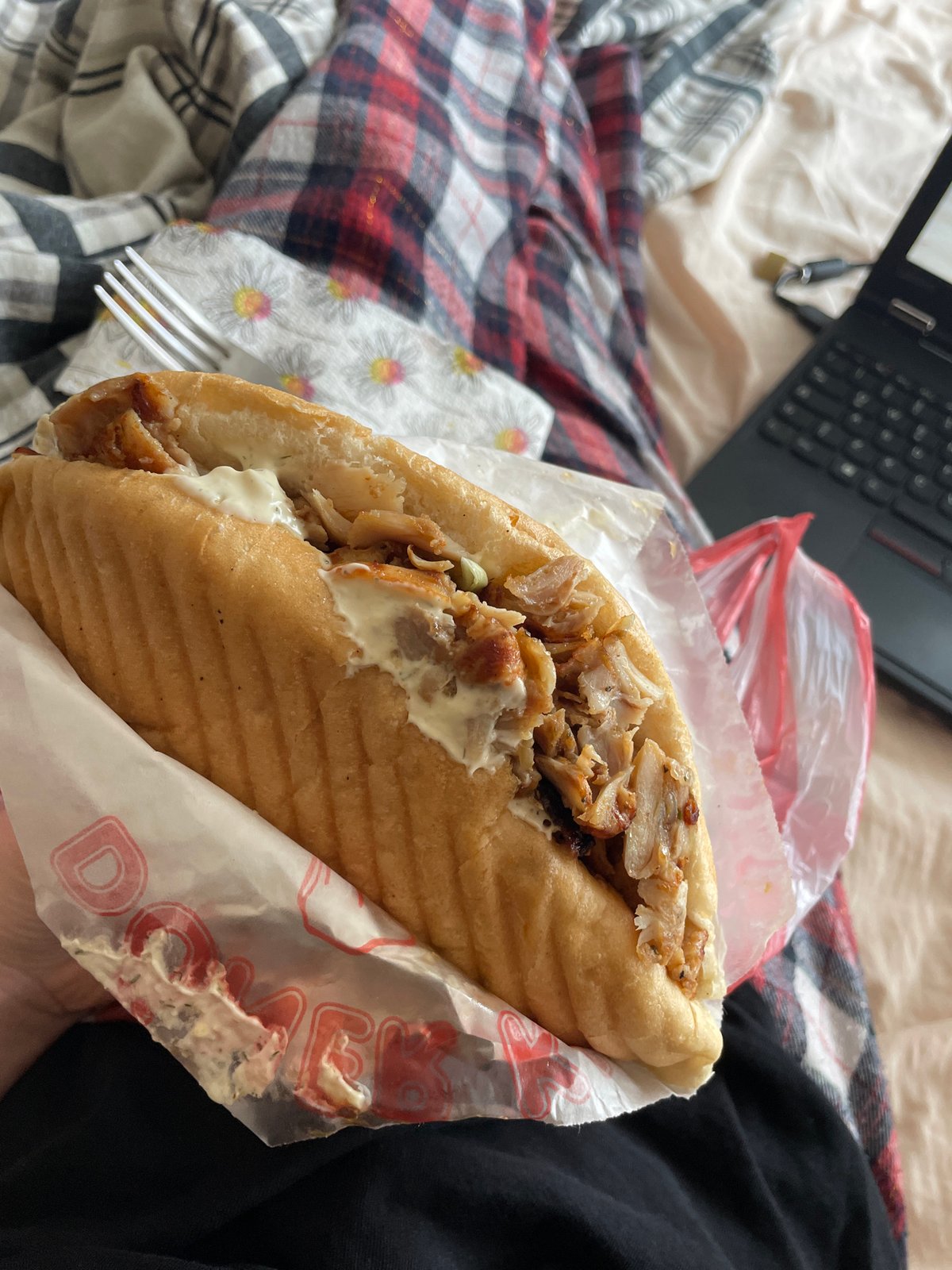 Person enjoys döner kebab lunch while watching laptop in bed