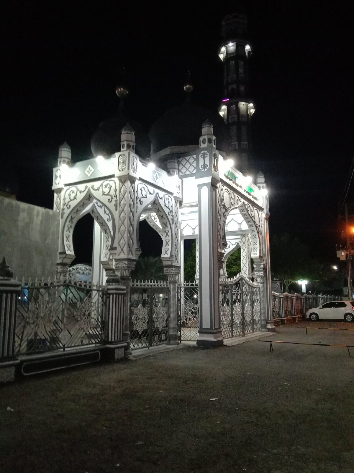 Evening street life captured around illuminated mosque in Indonesia
