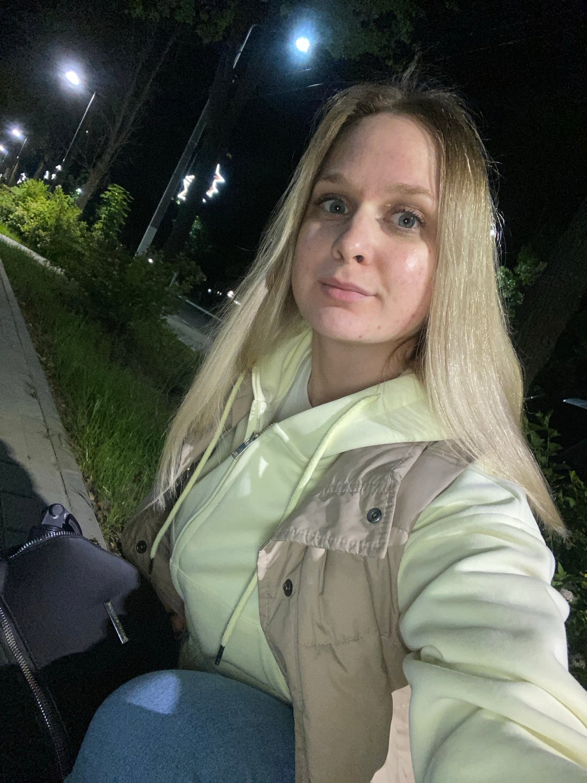 Woman takes nighttime selfies on illuminated walkway in Chaikovsky