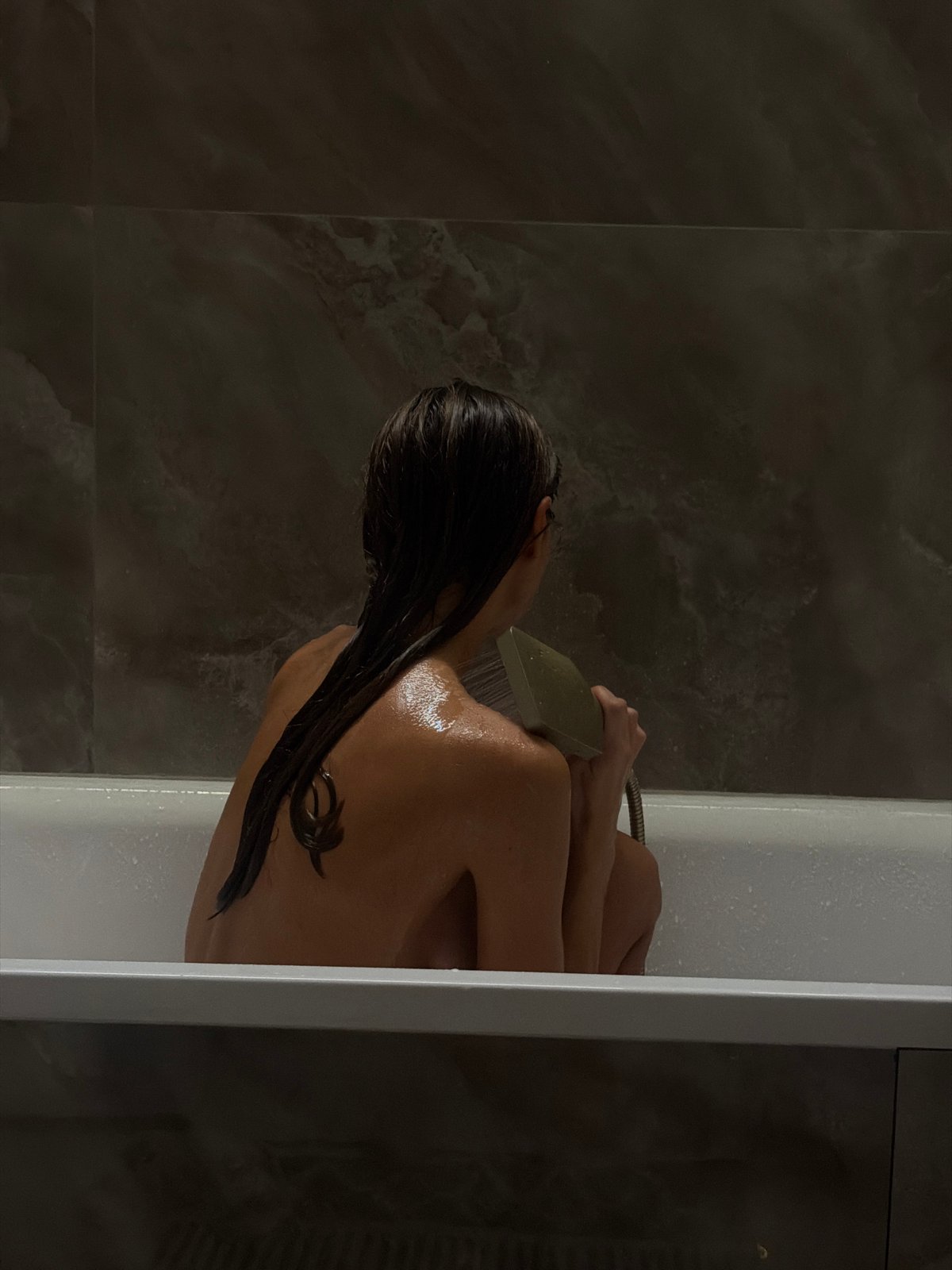 Person bathing with handheld shower in Krasnoyarsk bathroom