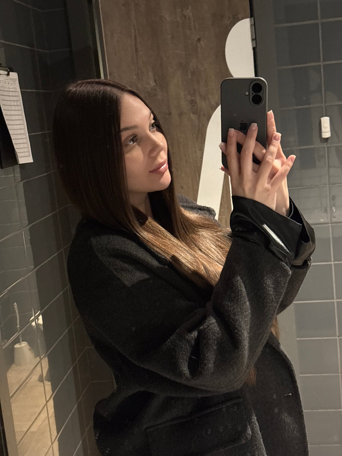 Woman takes selfie in gray coat at indoor location