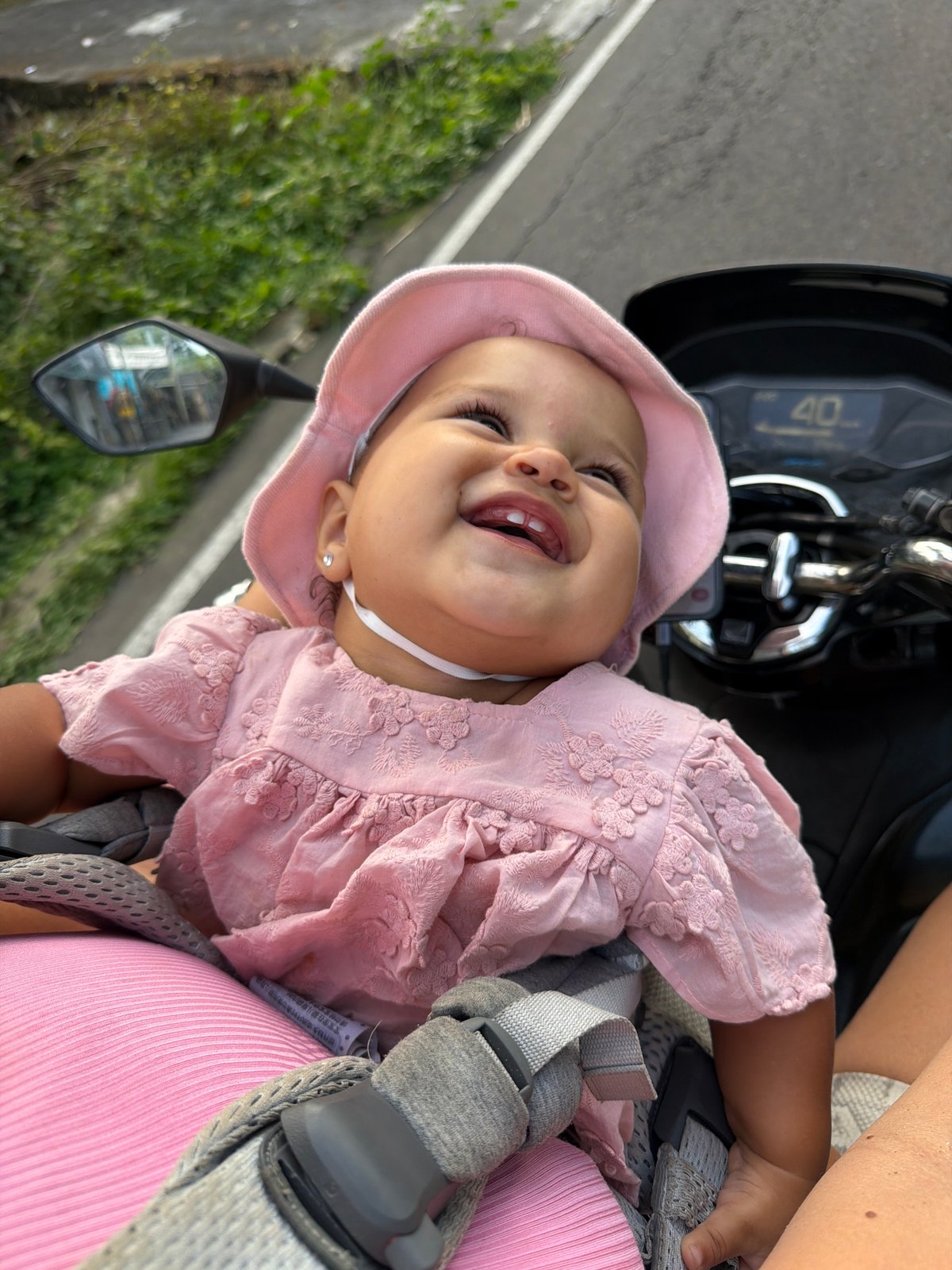 Infant in pink dress riding along in a scooter carrier, Sukawati