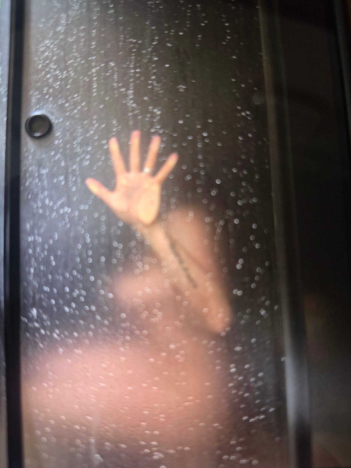 Figure observed behind wet glass surface, hand pressed against barrier