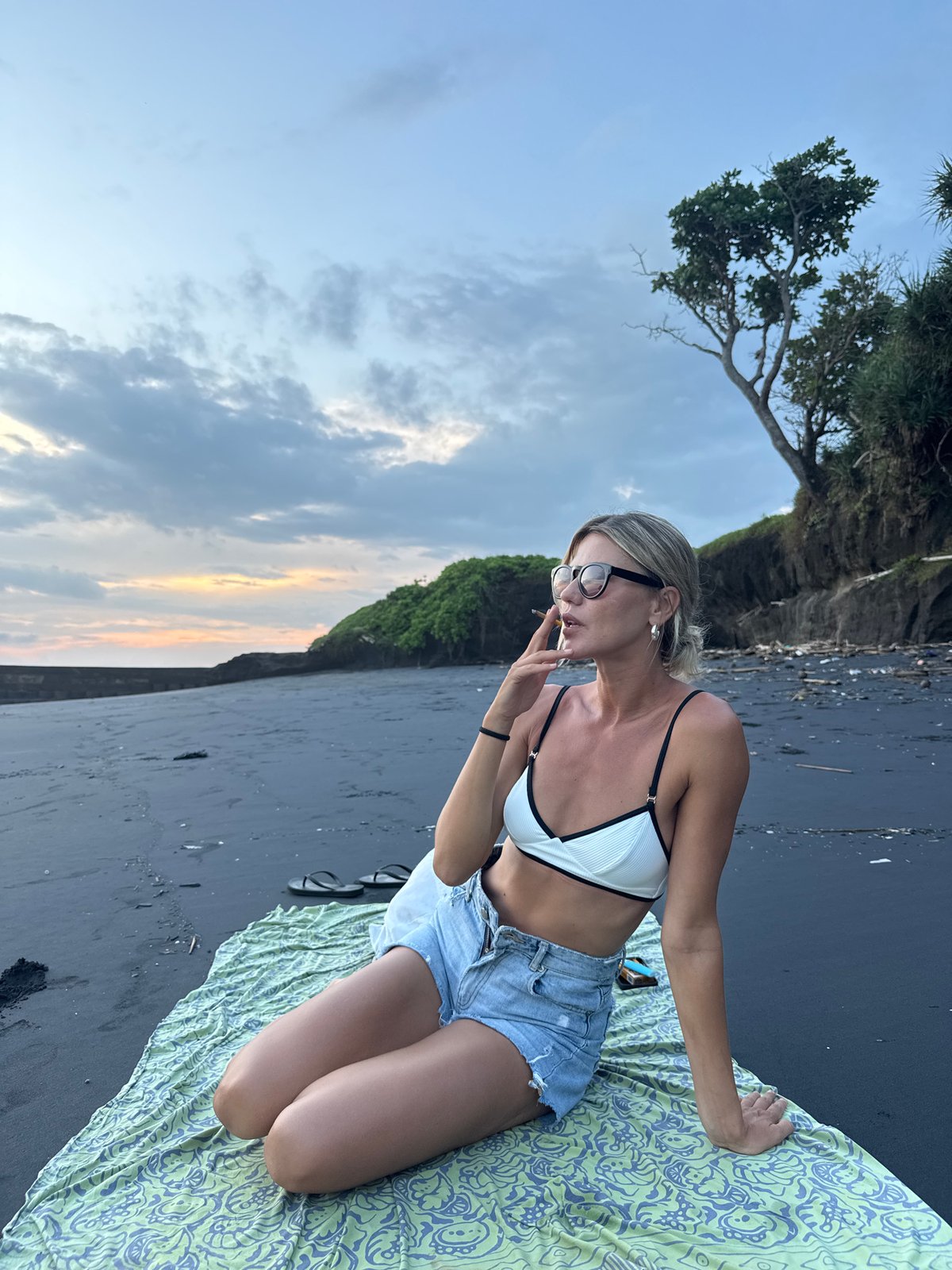 Woman smokes cigarette on black sand beach in Tabanan