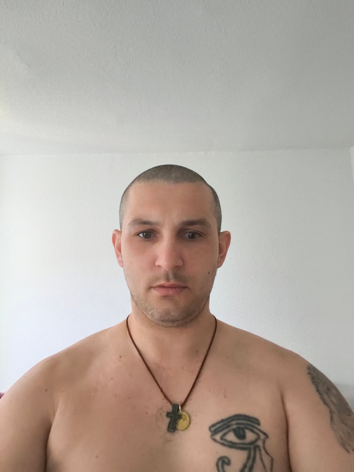 Indoor portrait session: shirtless, tattooed, cord necklace.