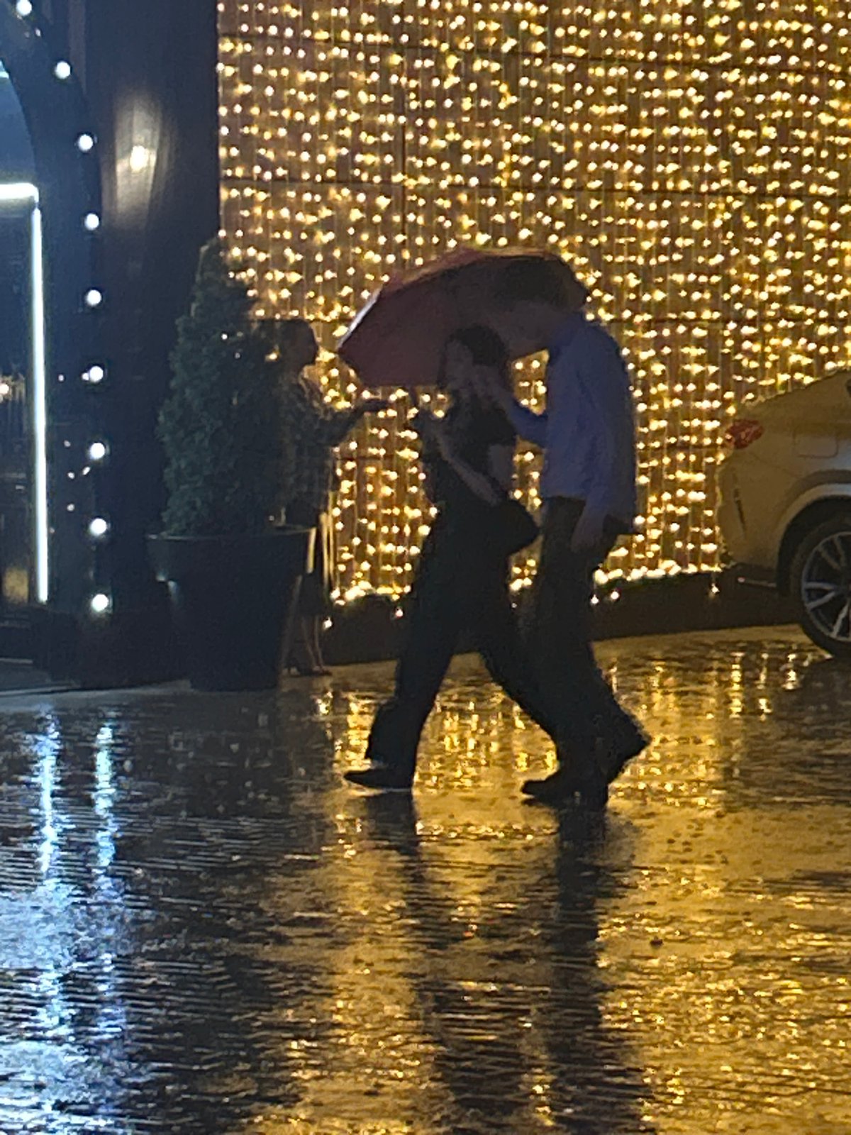 Nighttime rainstorm documented by witnesses sharing umbrellas, lightning