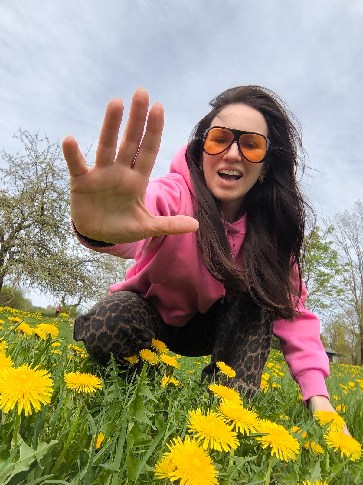 Woman in pink hoodie poses in Riga dandelion field
