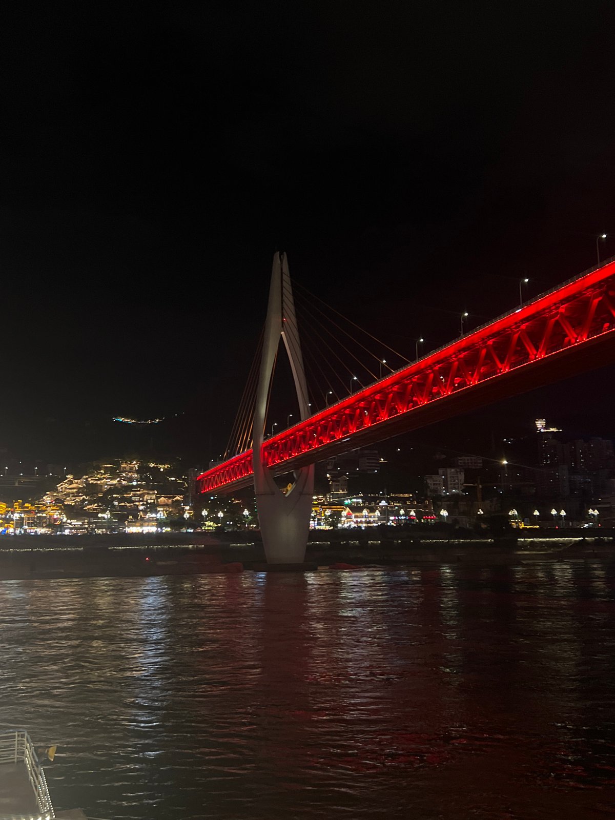 Chongqing's red-lit Hongyadong Bridge at night, cruise ship passing beneath