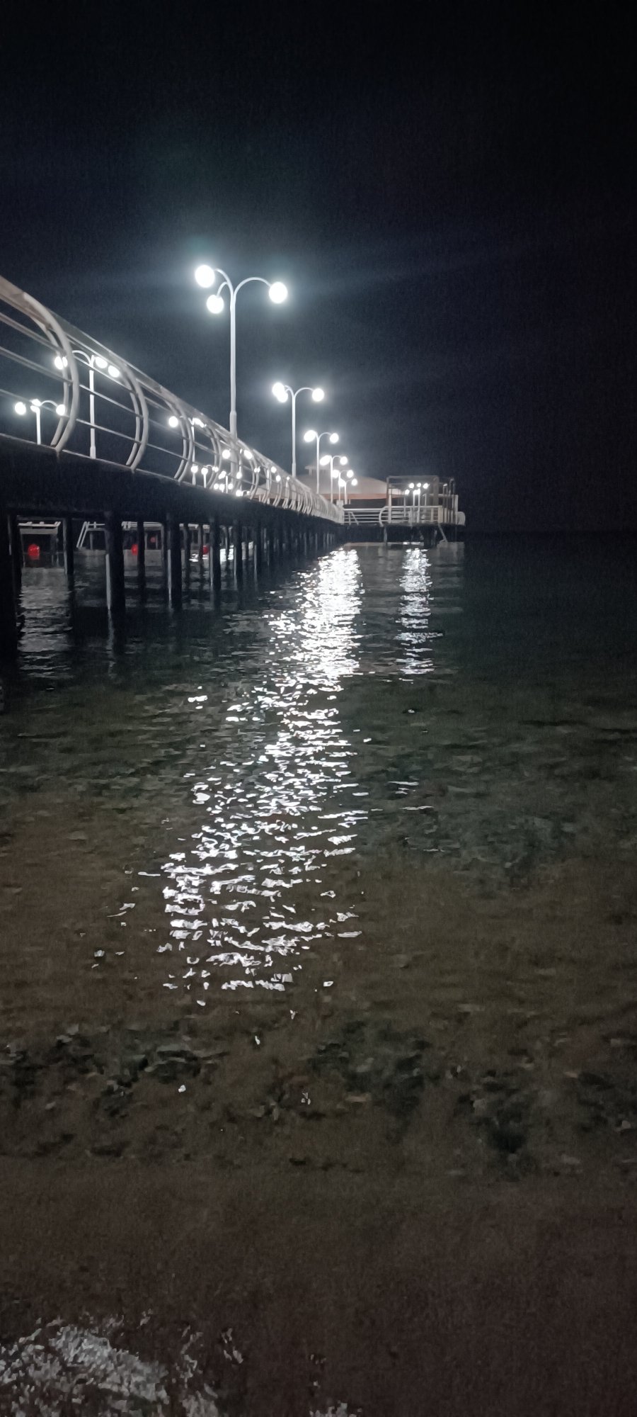 Full moon night over a calm sea and lit pier