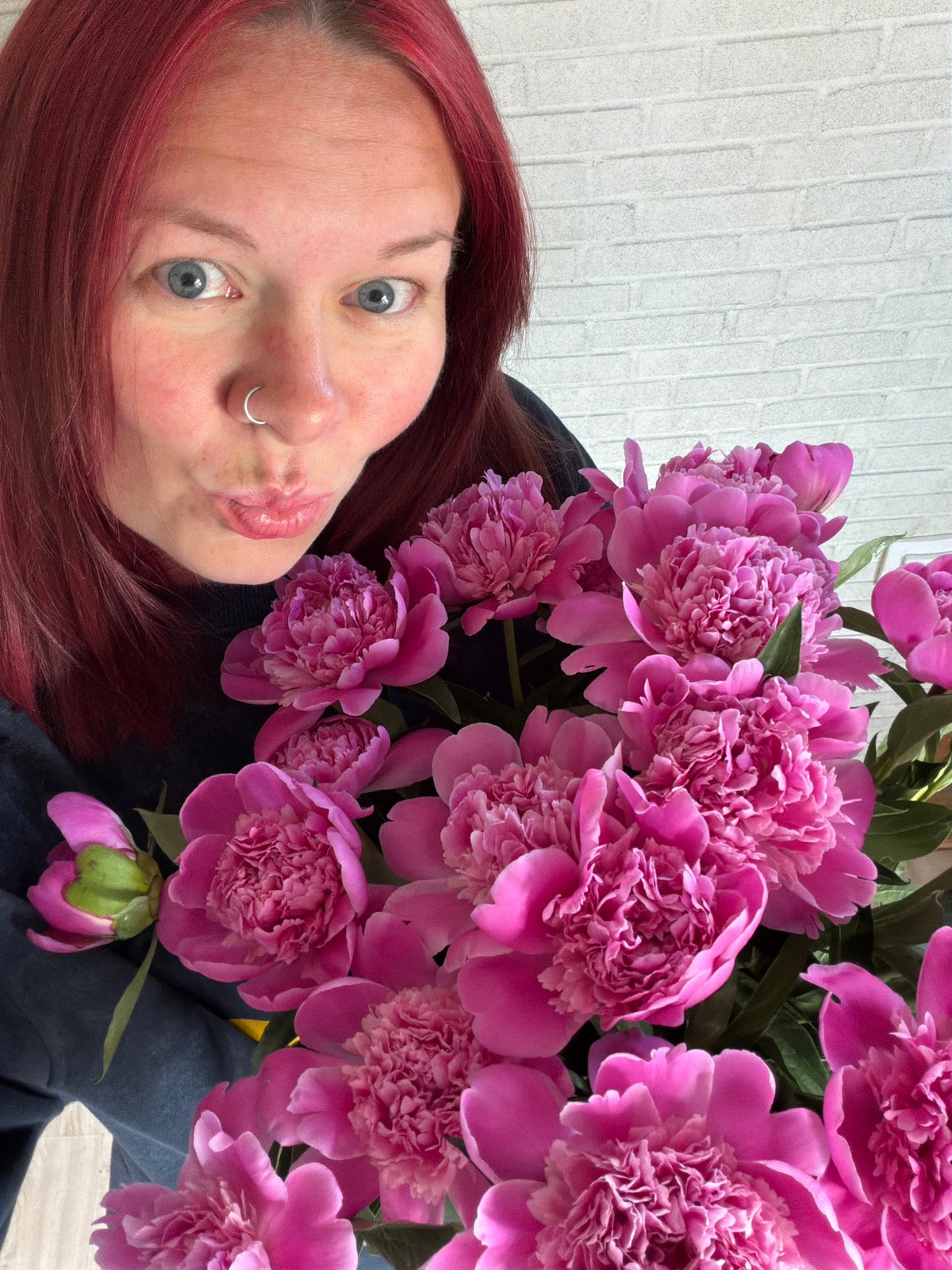 Woman poses with pink peonies against brick wall