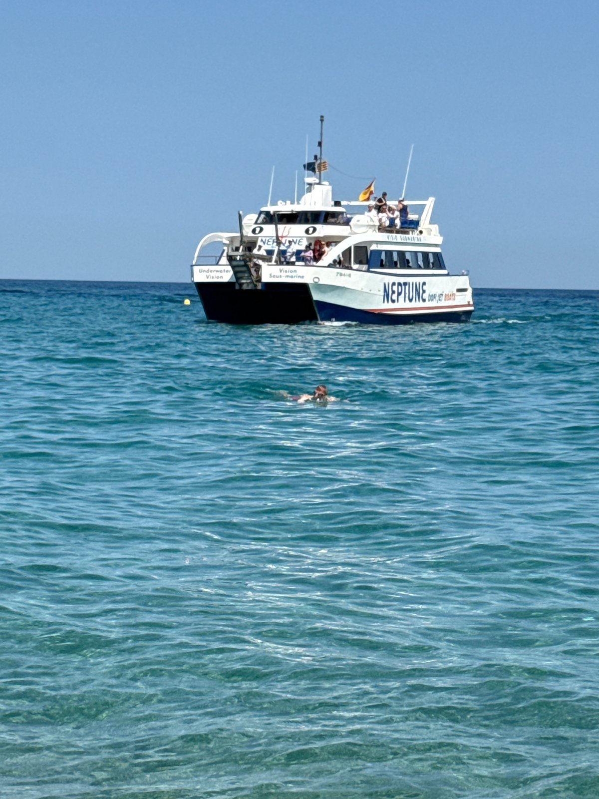 Neptune catamaran works the Blanes shoreline on a packed summer afternoon