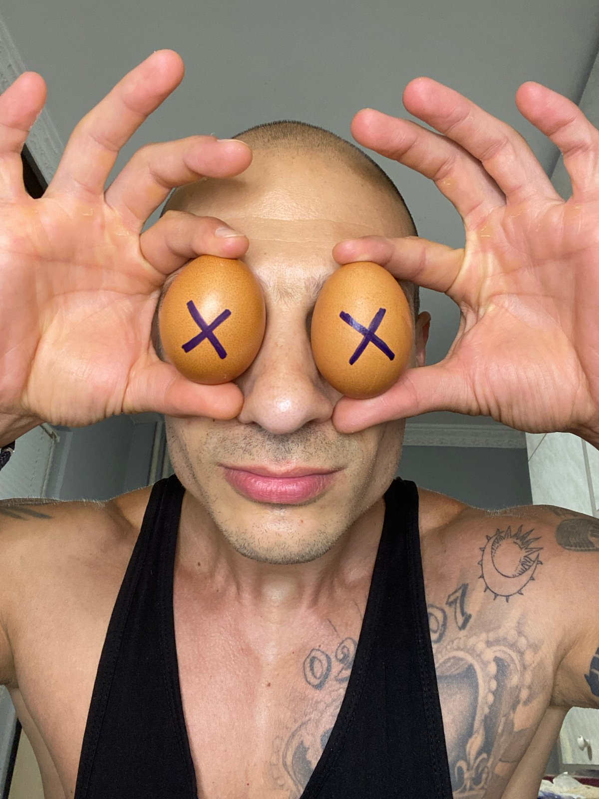 Tattooed person holds X-marked eggs over their eyes in Pleven