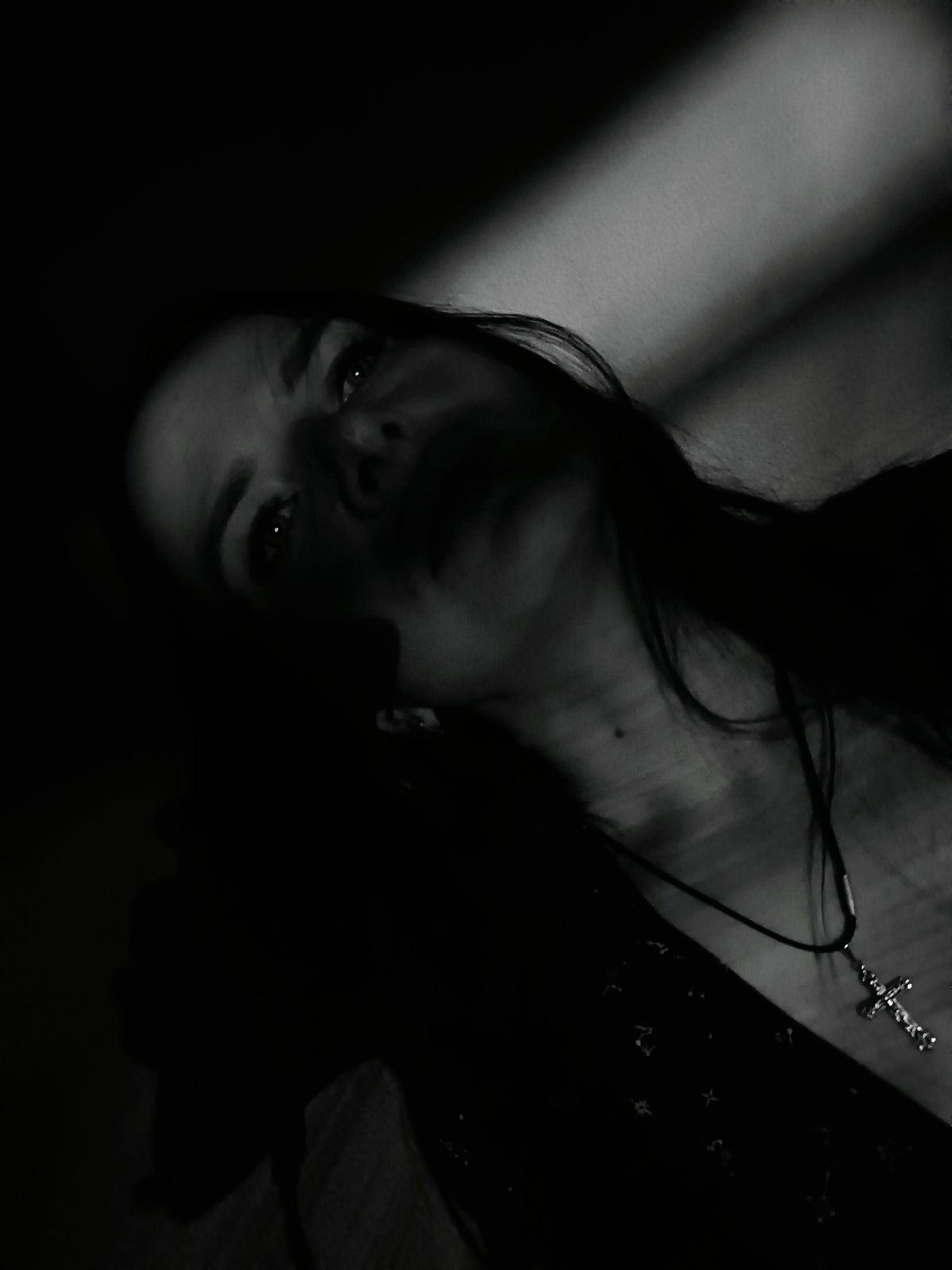 Person photographed in dramatic lighting wearing cross pendant