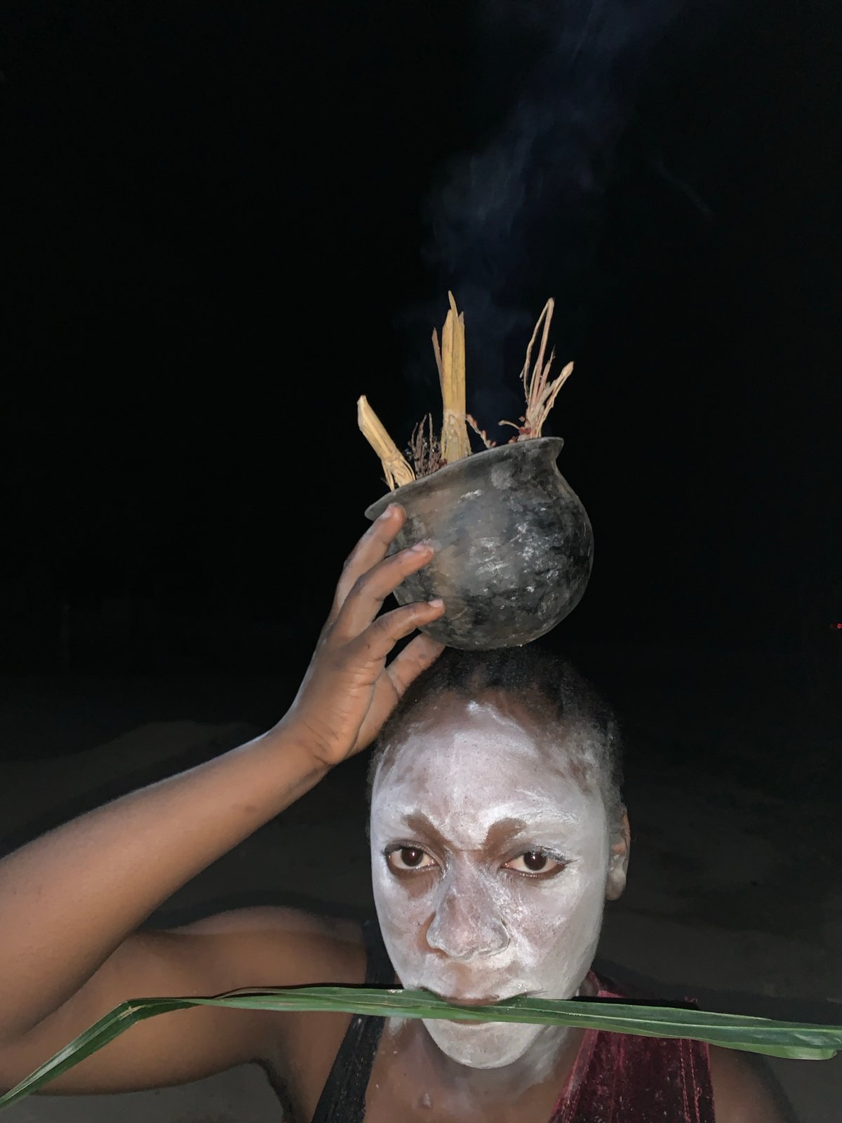 Person with white face paint holds smoking pot in Nigeria