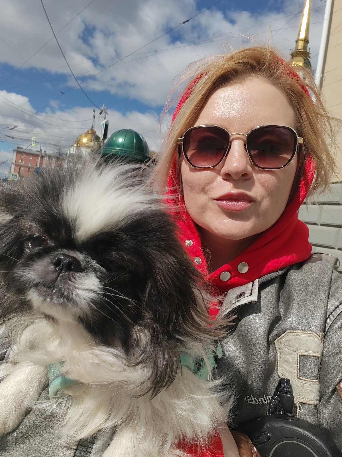 Woman walks Pekingese dog through Izhevsk landmarks on sunny morning