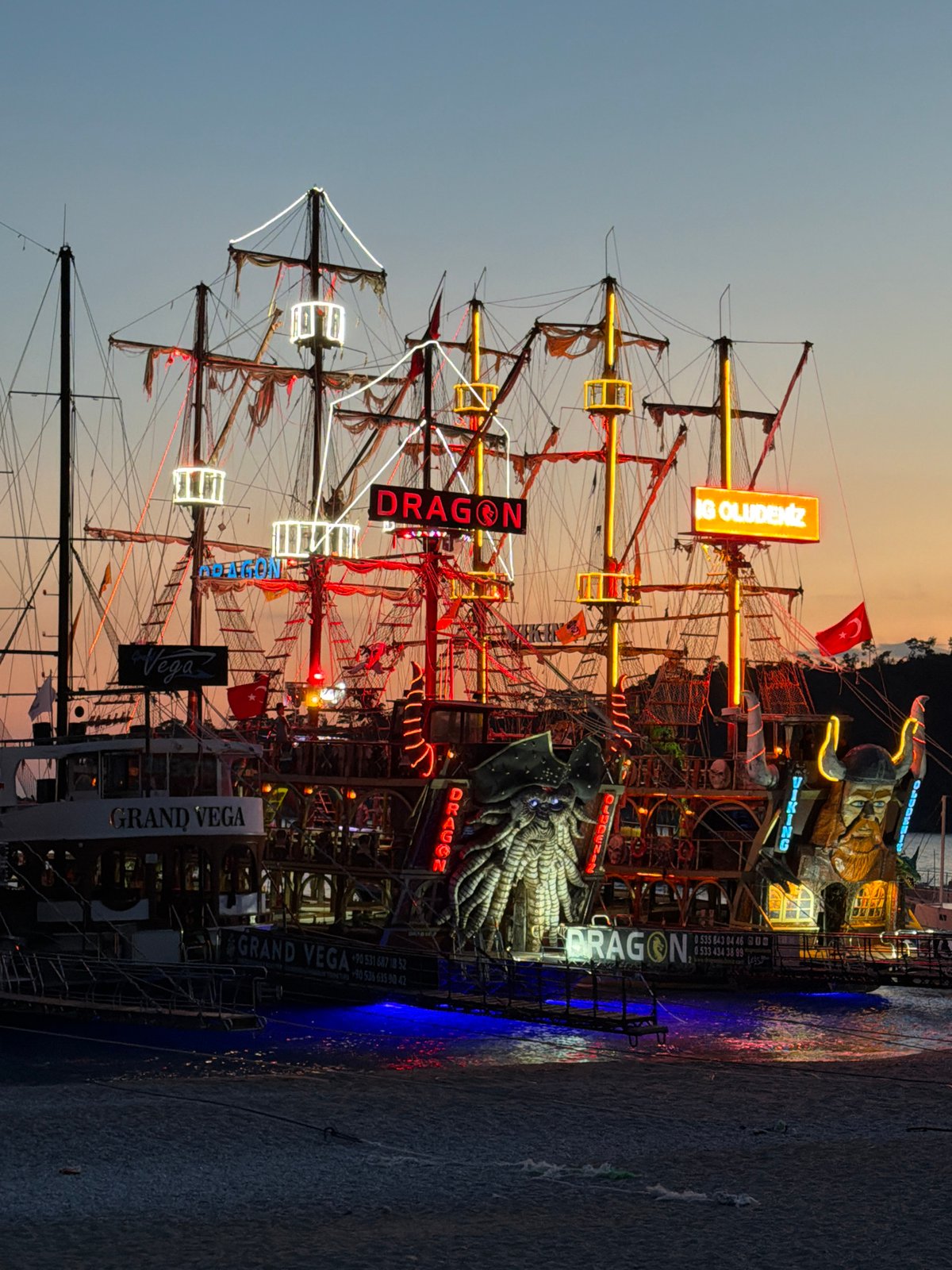 Illuminated tourist ships dock at Fethiye harbor during evening