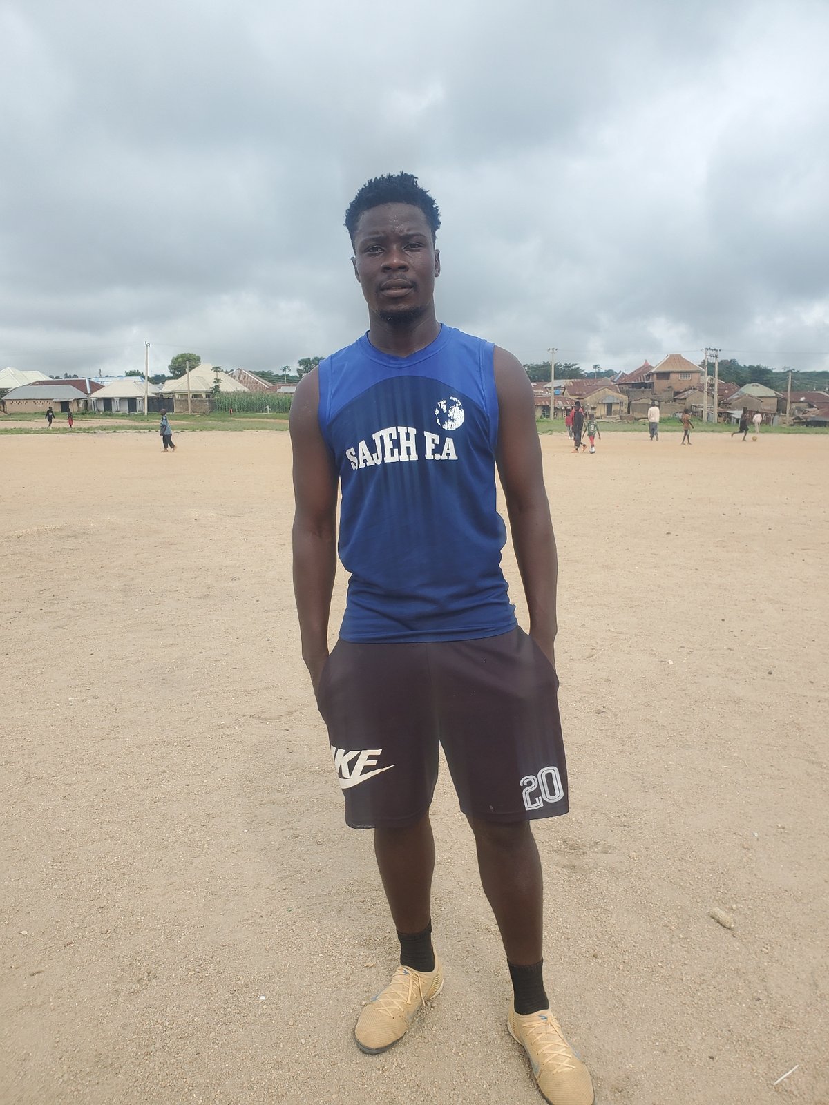 Standing on a dirt field in a 'SAJEH FA' sleeveless shirt