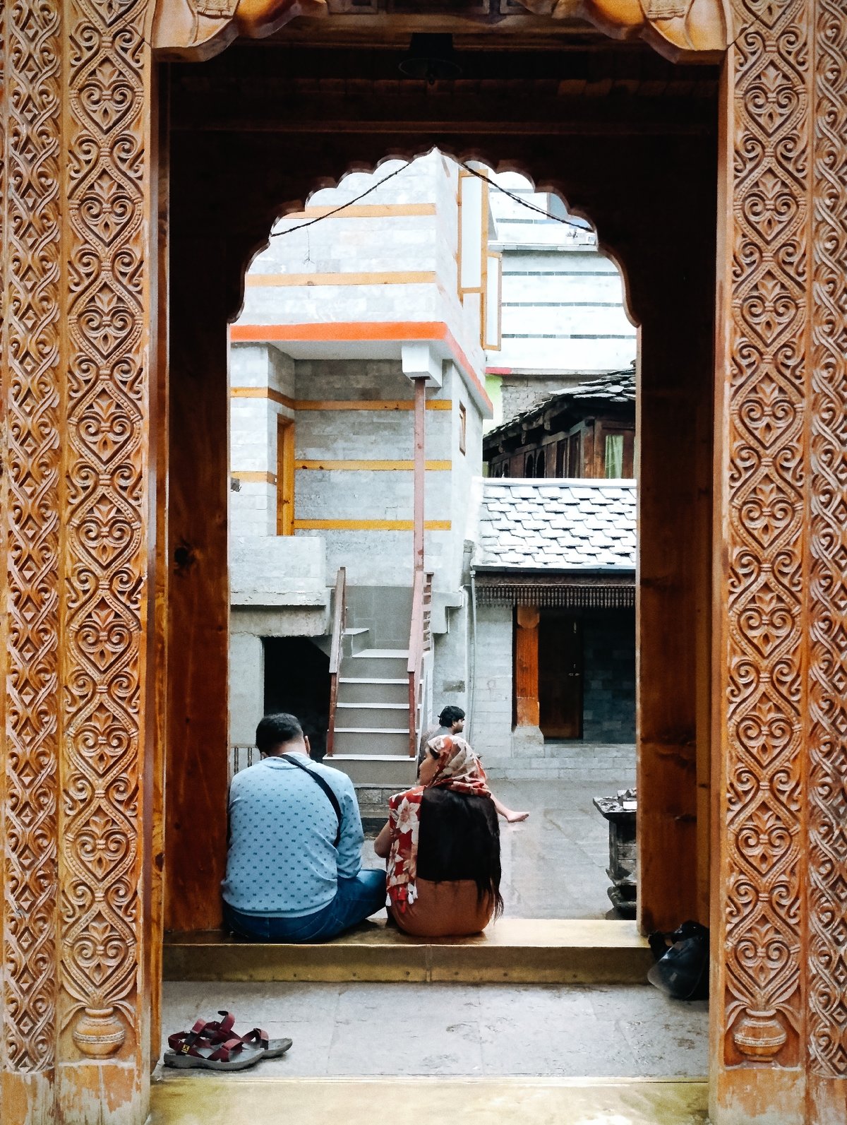 Sitting on temple steps beneath carved wooden archways in Vashisht