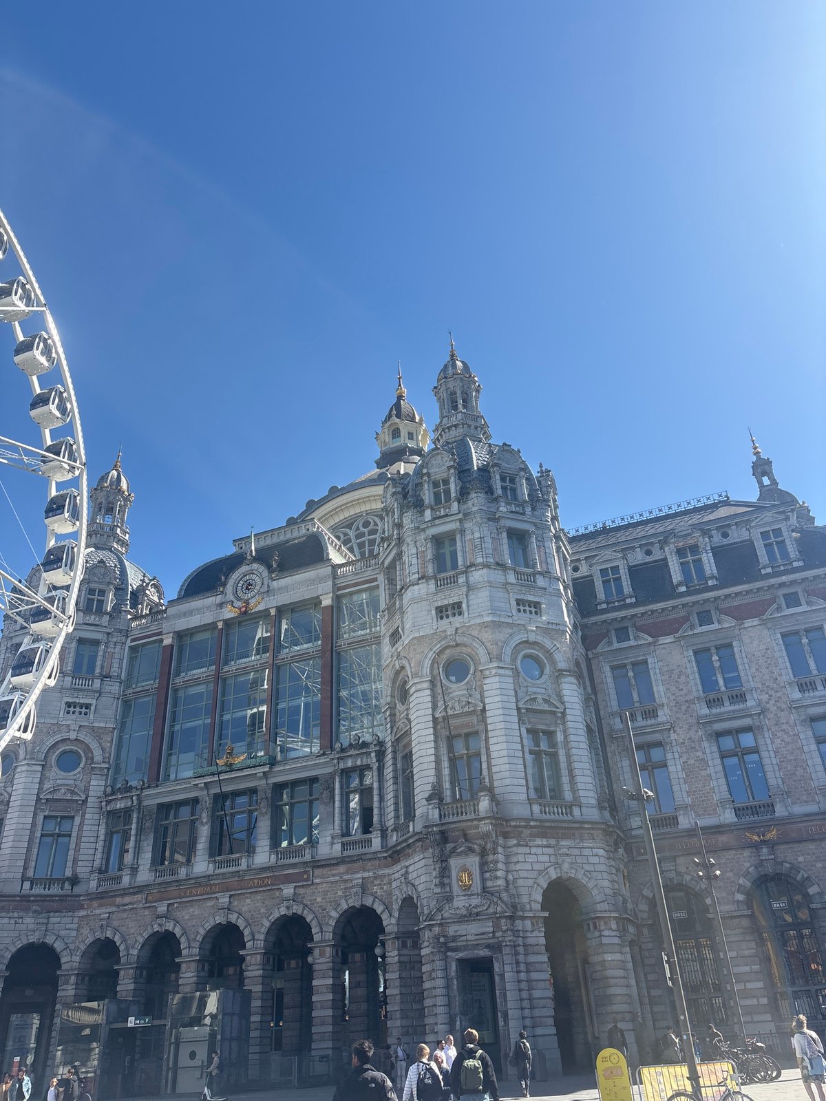 Historic Antwerp Central Station contrasts with modern Ferris wheel