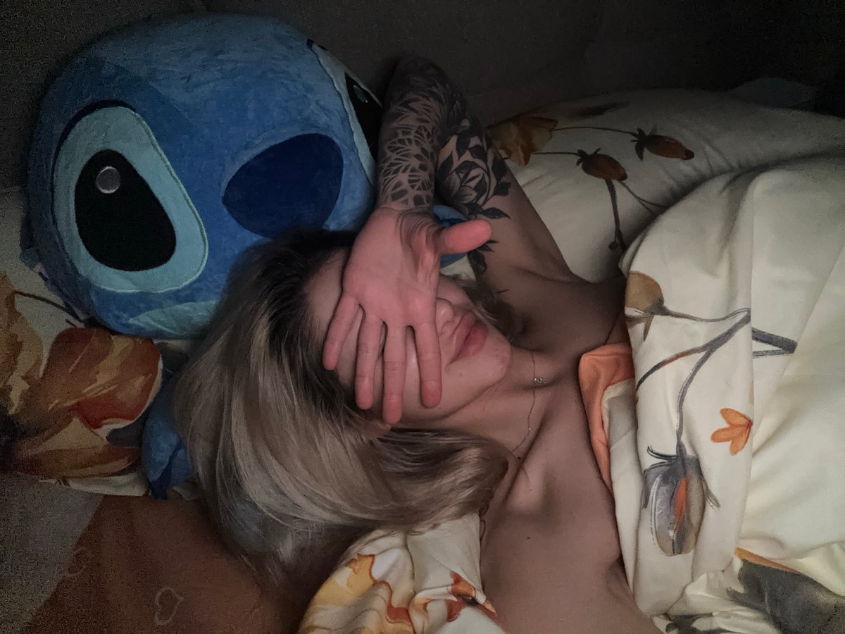 Person with tattoo rests in bed beside blue plush toy