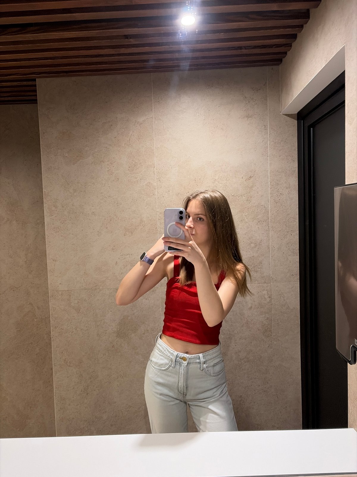 Mirror selfie in a Kyiv bathroom, red top and purple phone