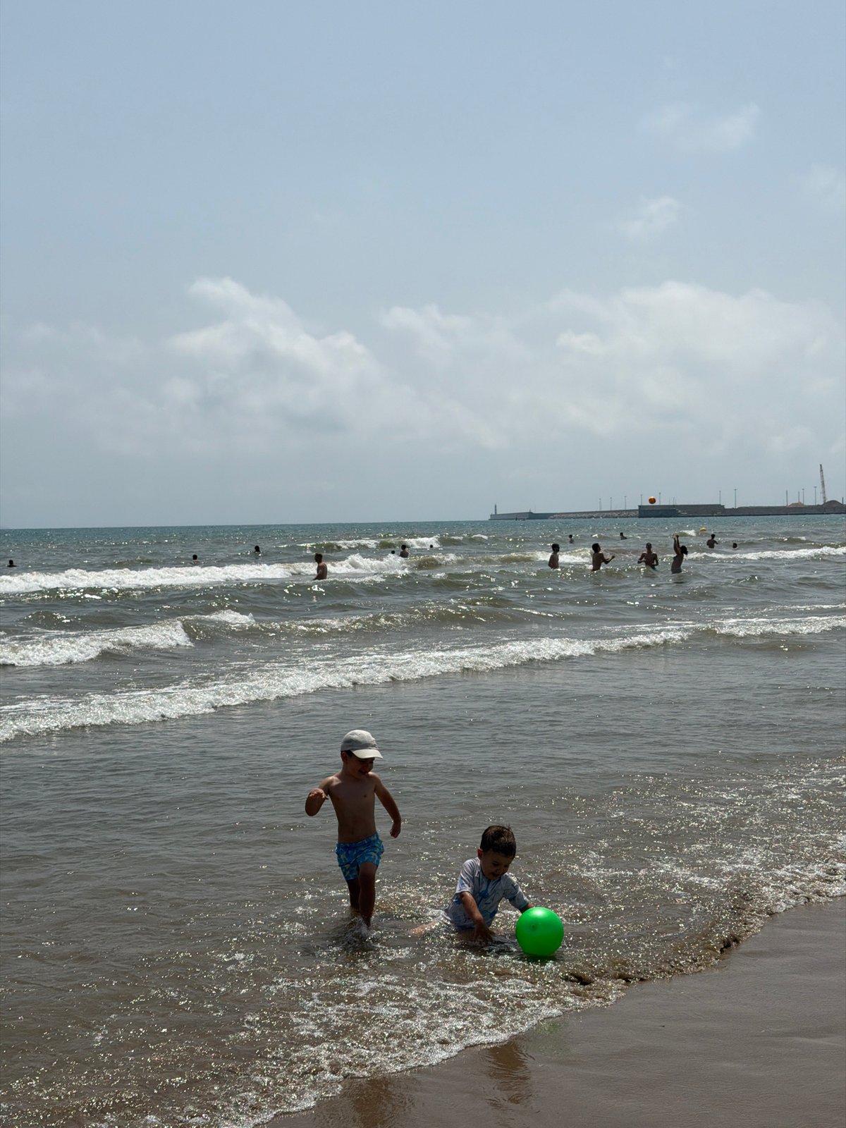 Crowded beach day with swimmers, kids, and street scenes nearby