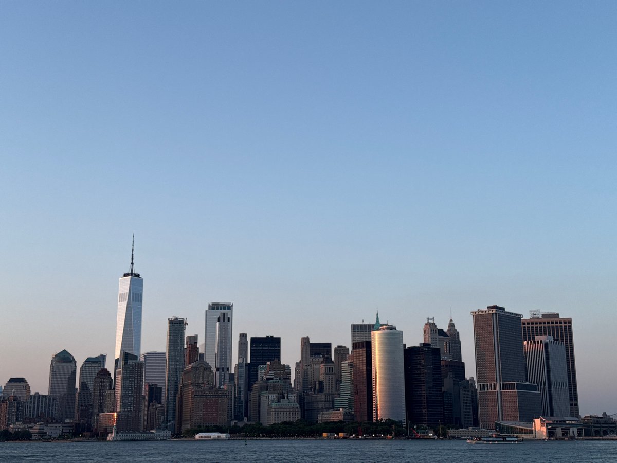 Lower Manhattan skyline glows at sunset around One World Trade Center.