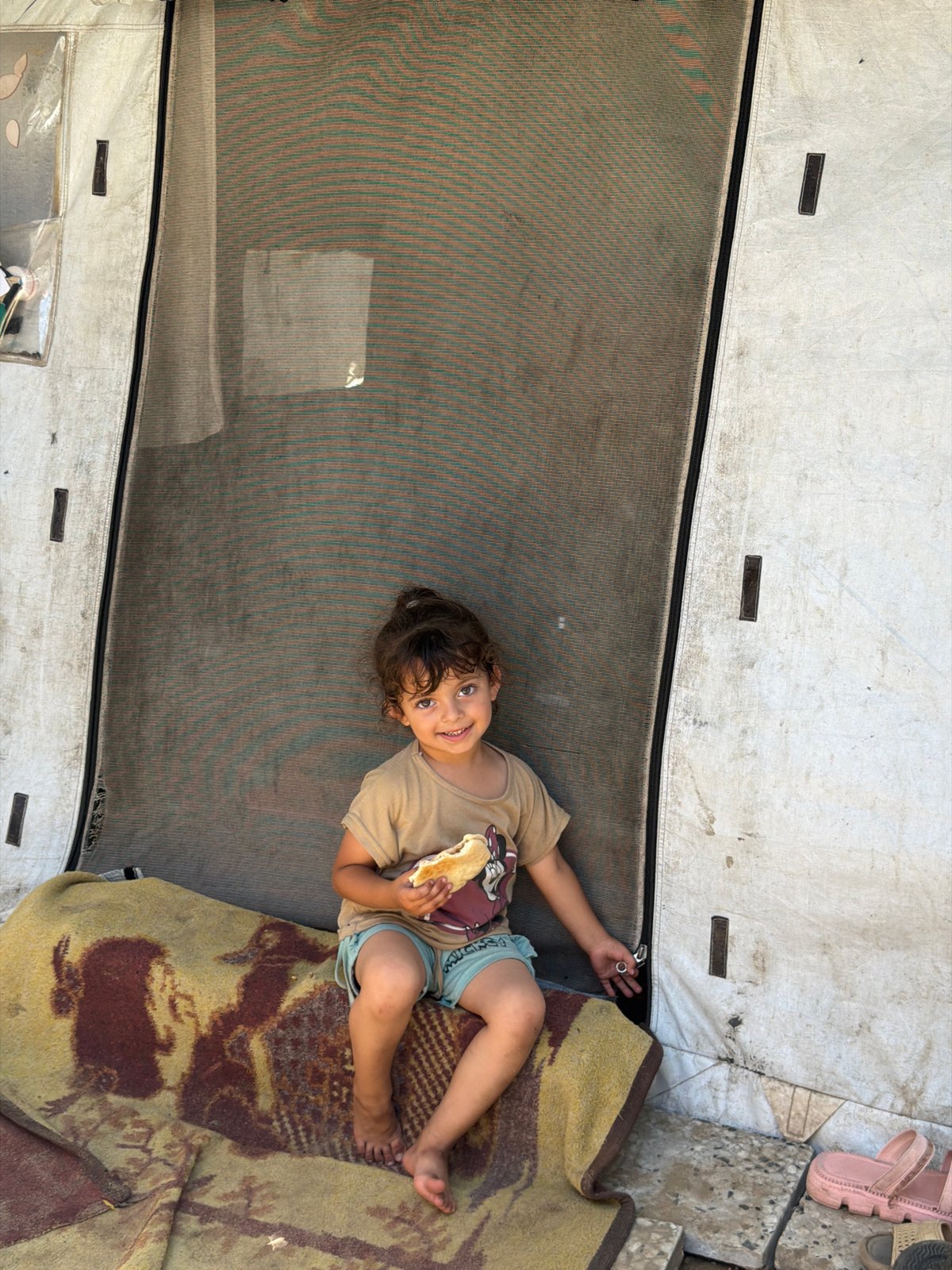 Child eats bread in tent shelter in Jabalia