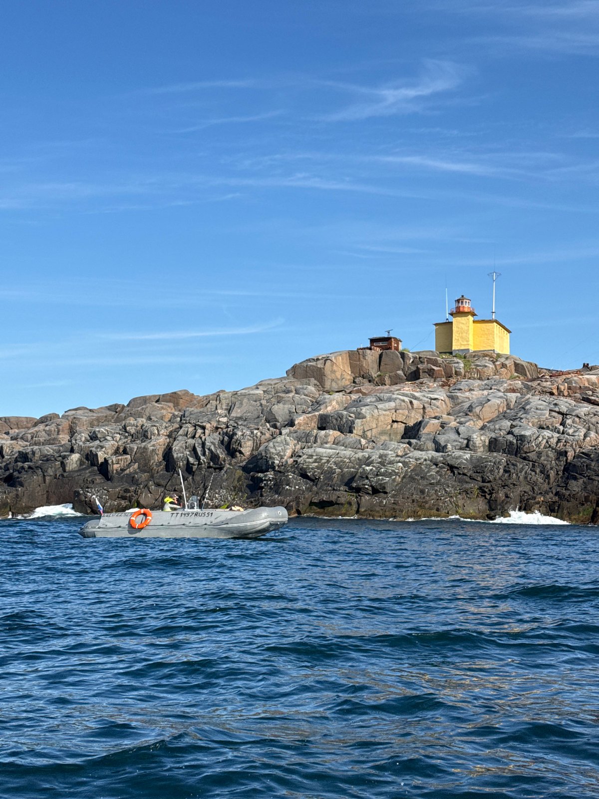 Yellow lighthouse on rocky Russian island, boats passing close