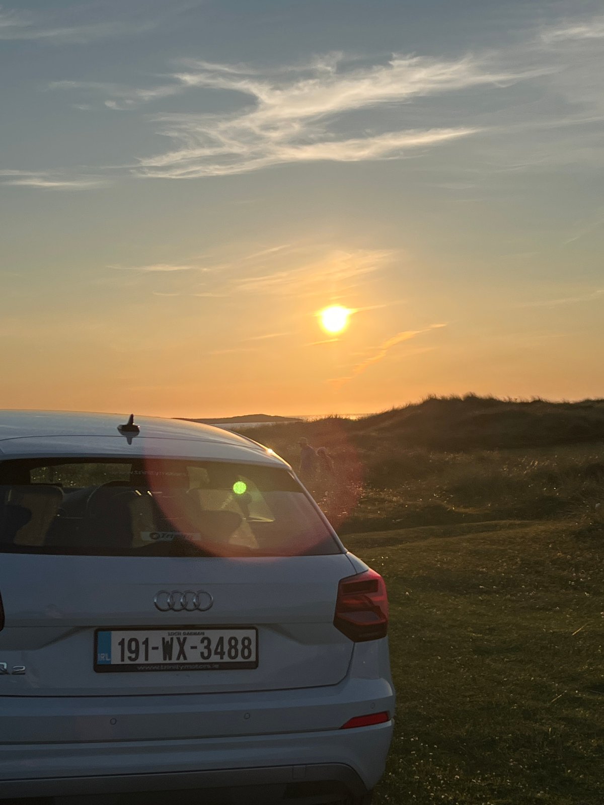 White Audi parked by Irish sand dunes at golden hour