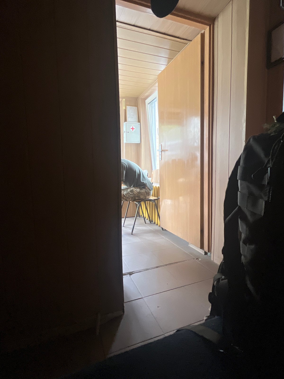 Inside a basic medical room, seated figure bent over near first-aid cabinet.