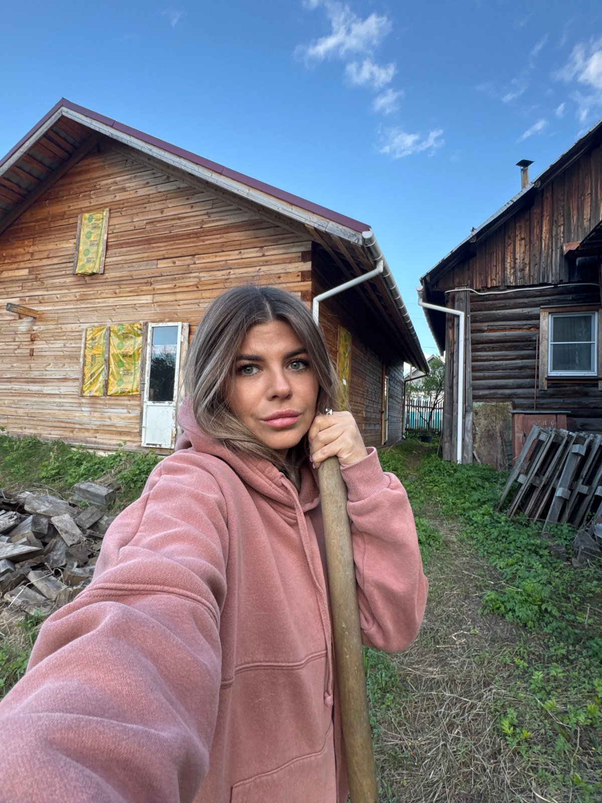 Woman takes selfies with shovel between wooden buildings in Russia