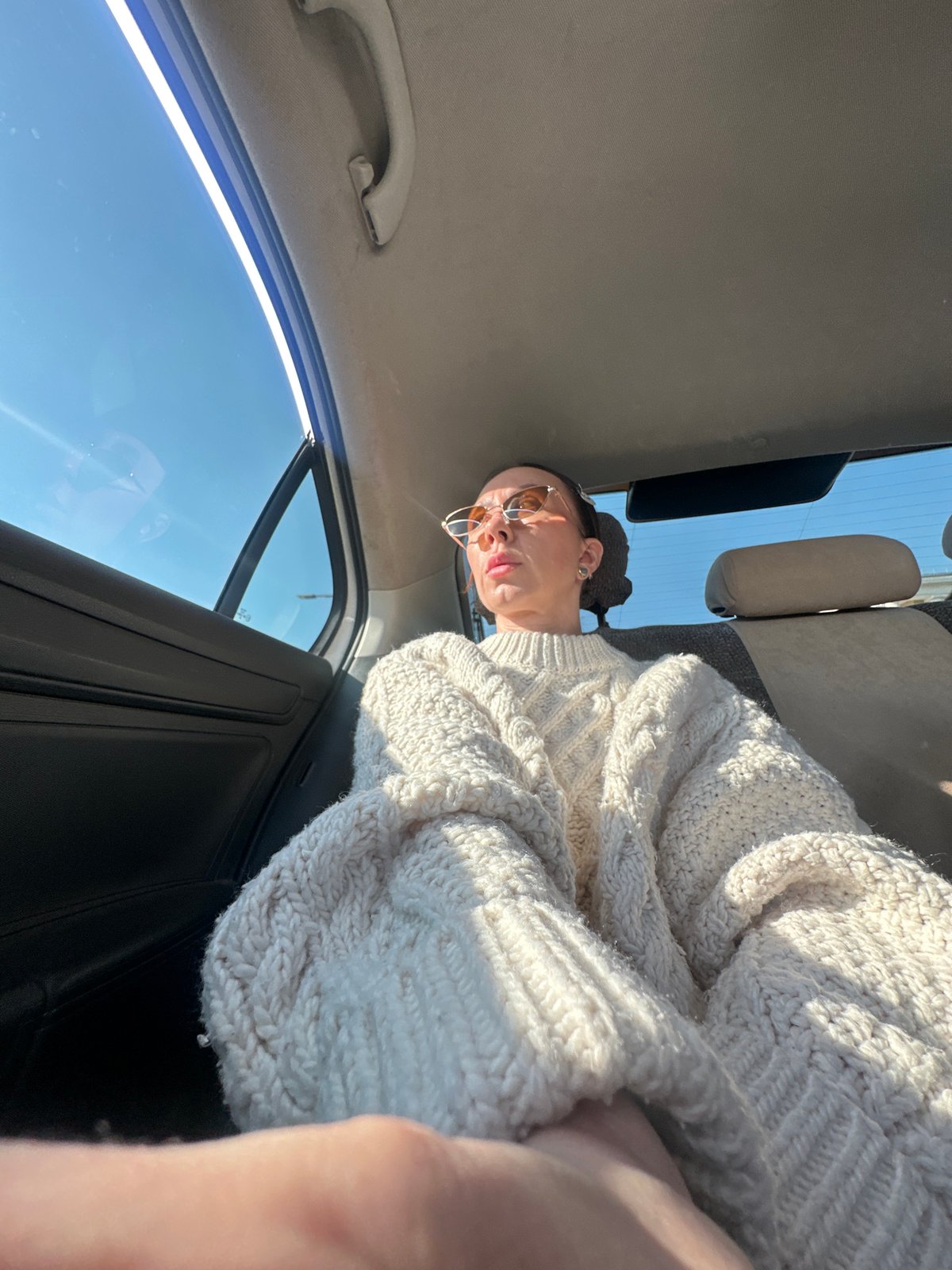 Person in sunglasses, white sweater photographed inside car in Votkinsk