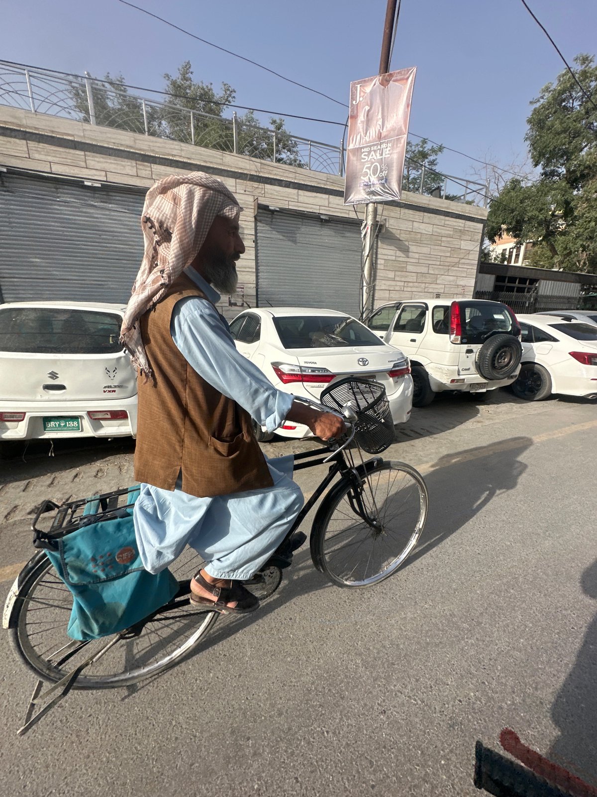 Elderly man cycles through busy Quetta street in traditional dress